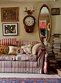 Gilt framed mirror and antique clock with striped sofa and artwork in Powys cottage, Wales, UK