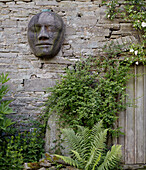 Carved face on exposed stone exterior at gate in Herefordshire garden, UK