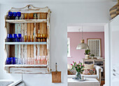 Collection of glassware on wall-mounted shelf with cut lilies viewed through doorway Tunbridge Wells home, Kent, UK