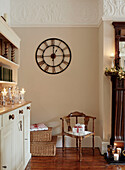 Wall mounted clock above antique chair in dining room with lit candles on dresser, UK home