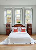Low double bed with wooden cabinets below triple window in Woodstock home, Oxfordshire, UK