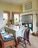 Gepunktete Tischdecke und Bank in gelber Landhausküche in einem Haus in Syresham, Northamptonshire, UK