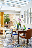 Retro chairs at table with tiled floor in conservatory extension of Deddington home, Oxfordshire, UK