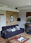 Faltbare Decke auf lilafarbenem Sofa mit freiliegender Steinwand in einem bretonischen Landhaus in Frankreich