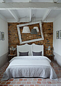 Double bed with exposed stone wall empty picture frame and lamps in Brittany cottage, France