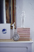 White ornaments and alarm clock with books on sideboard in Brittany cottage, France