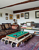 Kleiner Billardtisch auf Rollen mit braunem Ledersofa und bestickten Kissen in einem Bauernhaus in North Yorkshire, UK
