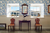 Antique wooden chairs and demi-lune table under square windows in North Yorkshire farmhouse, UK