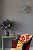 Bunter Stuhl mit Blumen auf Lederbeistelltisch und Glaswandleuchte in Londoner Wohnung, UK