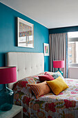 Verschiedene Kissen und eine tropische Decke auf dem Bett mit rosa Lampen in einer Londoner Wohnung, UK