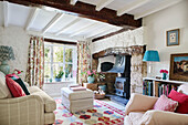Geblümte Vorhänge am Fenster mit Fußbank und Holzofen im Wohnzimmer von einem Cottage, UK
