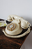 Cream rotary dial telephone on wooden side table in Colchester family home, Essex, England, UK