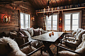 Cosy candlelit living room with comfortable seating with cushions and sheepskin and view of snow outside through windows of Wooden cabin situated in the mountains of Sirdal, Norway