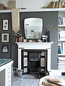 Vintage-Kamin und Spiegel mit Büchern im gedämpft grauen Wohnzimmer eines Hauses in Winchester, Hampshire, UK