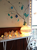 Lit candles and vase with leaf decorations on white console in family home, France