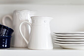 White ceramic jug and plates with blue ramekins on shelf in Reigate kitchen, Surrey, UK