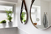 Zwei Spiegel hängen neben Zimmerpflanzen auf der Fensterbank und reflektieren das Badezimmer im Haus in Reigate, Surrey, UK