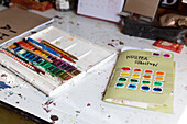 Paint box and pencils with colour chart on artist's desk Brighton, East Sussex UK