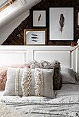 Attic bedrooom with double bed with copper bedside light and exposed brick wall displaying feather artwork multi-textured pillows in cotton linen and fake fur Cardiff Wales UK