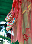 Ein Paar gestreifte Espadrilles hängen an einem Schuppen mit rosa Voile-Stoff