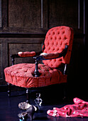 Ein abgenutzter Sessel im Vintage-Stil in einem dunkel getäfelten Raum mit Kleidung und Schuhen auf dem Boden