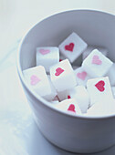 Pink hearts printed on white sugar lumps in a bowl