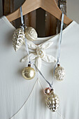 Weißes Abendkleid auf einer Leiter mit silbernen und goldenen Weihnachtskugelgirlanden als Detail