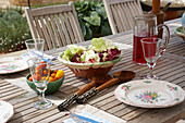 Salat und Tomaten mit Weingläsern und Blumentellern bei einem Essen im Freien, Lincolnshire, England, UK