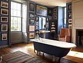 Blue freestanding roll-top bath in sunlit bathroom with artwork, Georgian townhouse, Laughame, Wales, UK