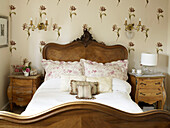 Carved antique bed and floral wallpaper in country house Suffolk, England, UK
