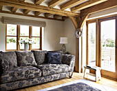 Floral gemustertes Sofa im Wohnzimmer mit Balken in einem Landhaus in Gloucestershire, England, UK