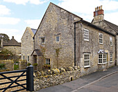 Dry-stone wall with gate to side entrance of stone Gloucestershire house, England, UK