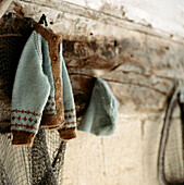 A Children's knitted cardigan and hat hanging on a period beam in a cloakroom