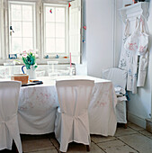 White light dining room with loose covers on dining chairs and table cloth on table stone floors and a large window