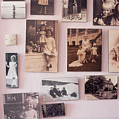 Display of old family black white and sepia photographs hung on a light purple painted wall in a hallway