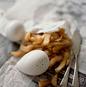 Portion of chips wrapped in newspaper with salt and pepper pot