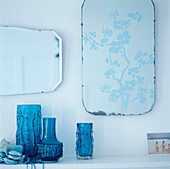 Detail of turquoise blue glass vases on a shelf with mirrors displayed on the wall