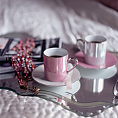 Zwei rosafarbene Kaffeetassen auf einem Spiegeltablett, das auf einem Bett steht