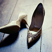 Paar elegante goldene Schuhe mit hohen Absätzen, die auf einem dunklen Holzboden ausgezogen werden