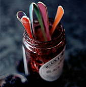 Detail of an empty blackberry jam jar full of spoons