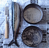 Filetierter Fisch auf Zeitungspapier mit Kochgeschirr im Vintage-Stil