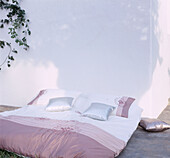 Doppelbett mit Bettwäsche draußen auf einer sonnigen Terrasse im Garten