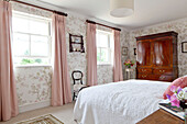 Pink curtains at sash windows in bedroom with polished wooden antique wardrobe in Wiltshire country house England UK