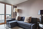 Grey corner sofa in beige living room with view of lake in British home, England, UK