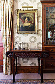 Carved side table with Oak Garland Wallpaper and bookcase in historic Somerset country house UK