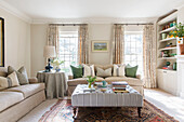 Striped ottoman and sofas with sunlit windows in London living room UK