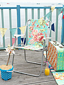 Floral patterned folding chair with vintage suitcase on coastal decking with bunting