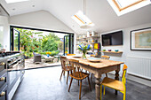 Wooden table and chairs below skylight windows with open doors to terrace from Reading kitchen Berkshire England UK
