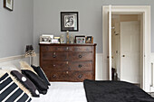 Schwarzer Bettbezug mit kontrastierenden Kissen und antiker Kommode im taubengrauen Schlafzimmer