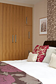 Blumenmustertapete und Bettdecke in einem Londoner Schlafzimmer mit Einbauschränken